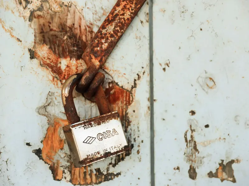 Close-up of a rusty padlock on a weathered wall, showcasing vintage charm.