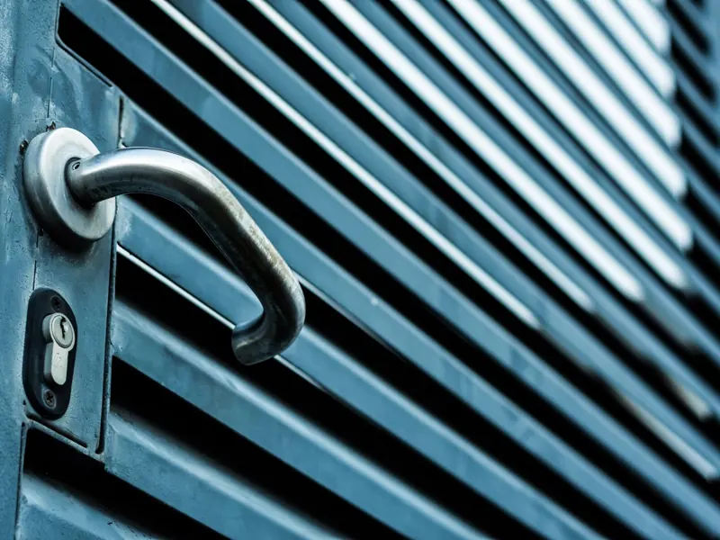 Close-up of a sleek stainless steel door handle and lock on a blue metallic door.
