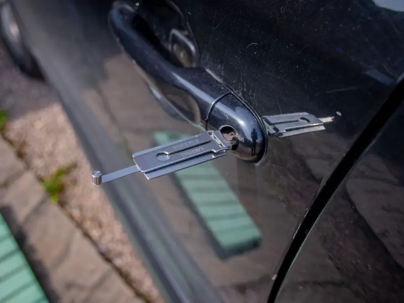 Close-up of a locksmith tool inserted into a car door lock, demonstrating security access.