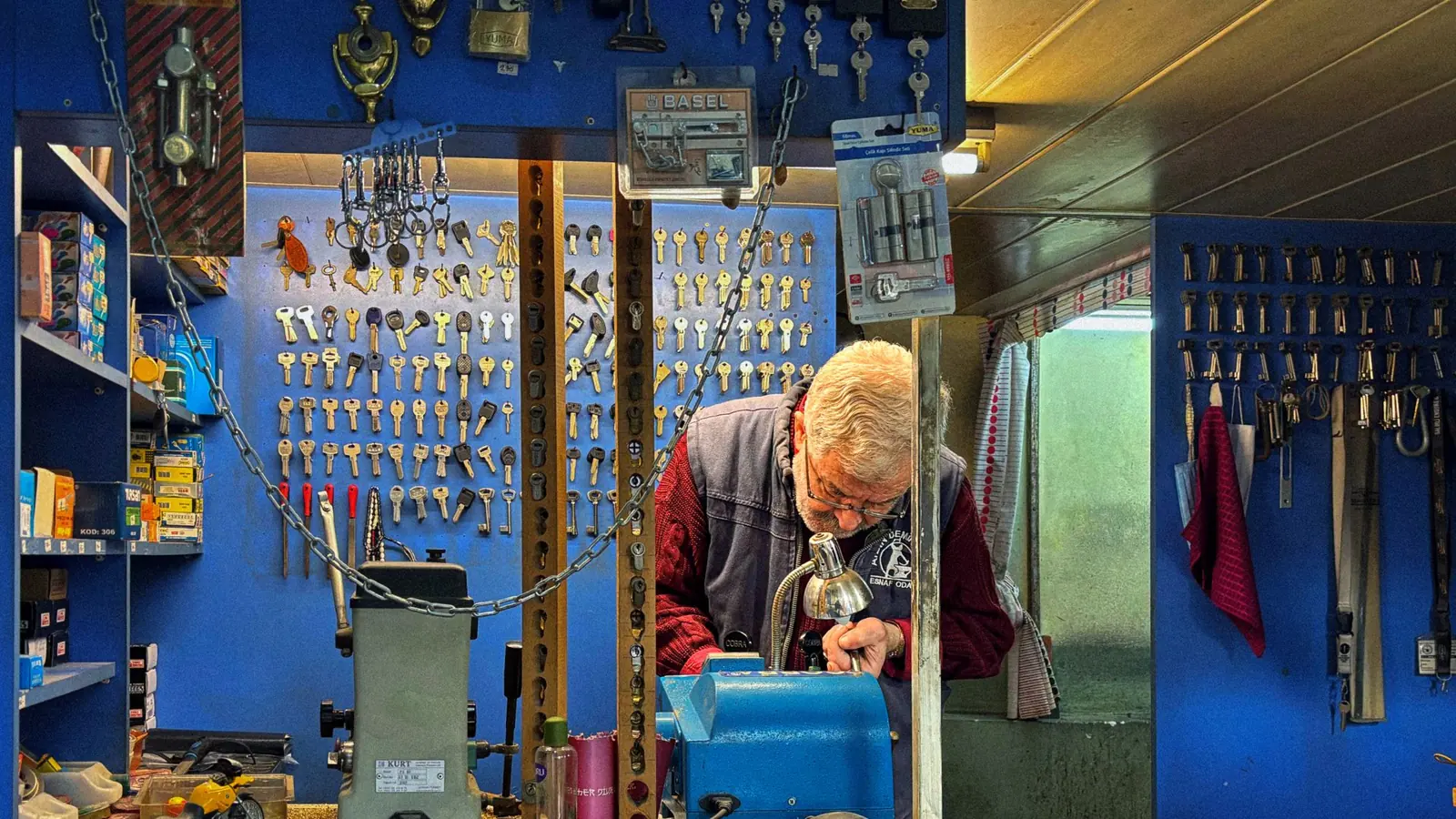 A senior locksmith crafts a key in his hardware shop filled with locks and keys.
