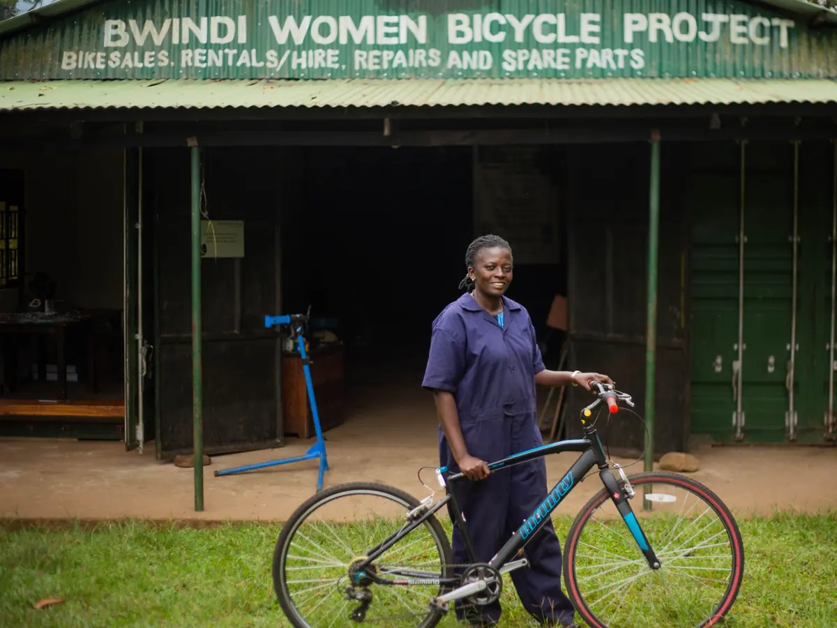 A woman stands proudly with a bicycle at Bwindi Women Bicycle Project. Empowerment and community development.