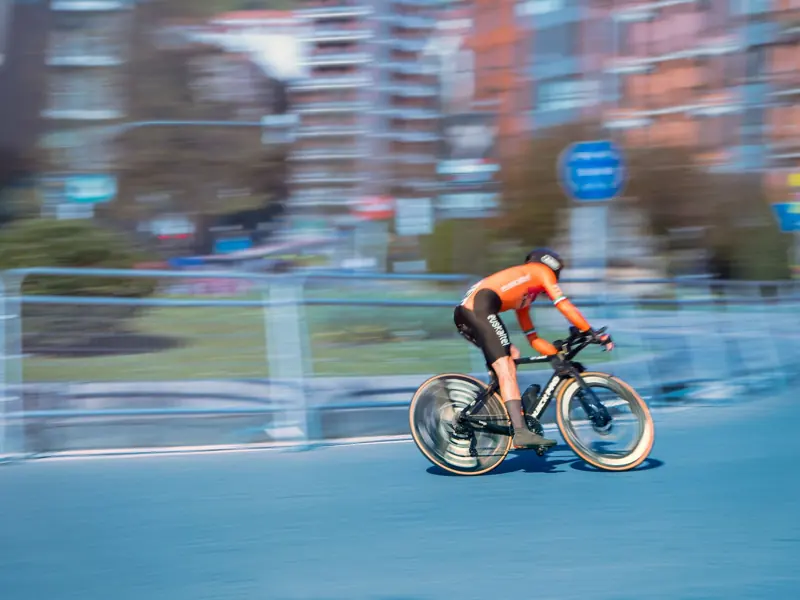 Blurry cyclist races through city streets wearing orange sportswear.