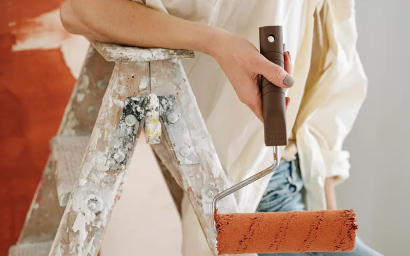 A close-up of a person using a roller to paint a wall during renovation.