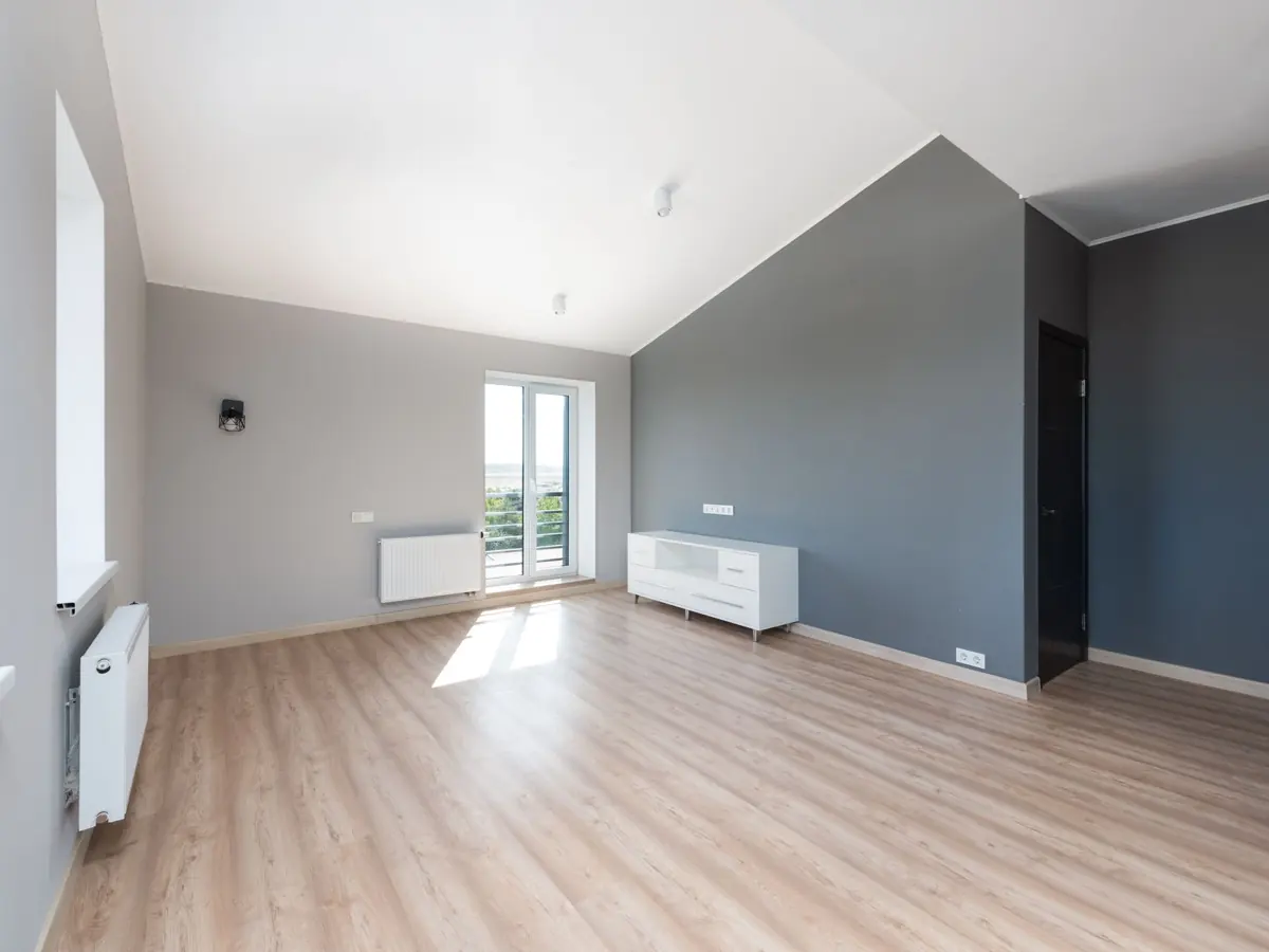 Wide-angle shot of a modern unfurnished apartment with wooden flooring and large windows.
