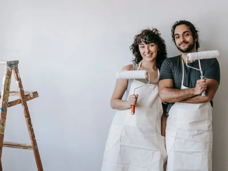 A cheerful couple with paint rollers ready for a home makeover, embodying creativity and teamwork.