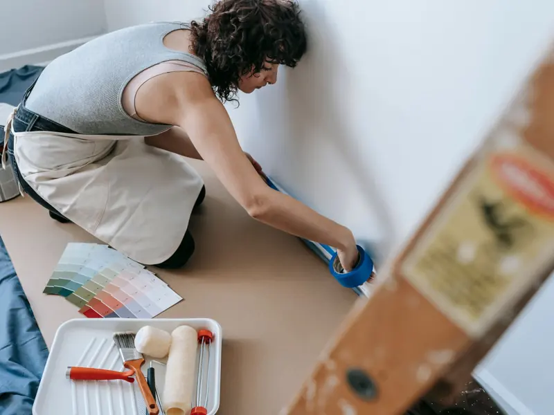 Female using blue tape for home painting project in a modern apartment.
