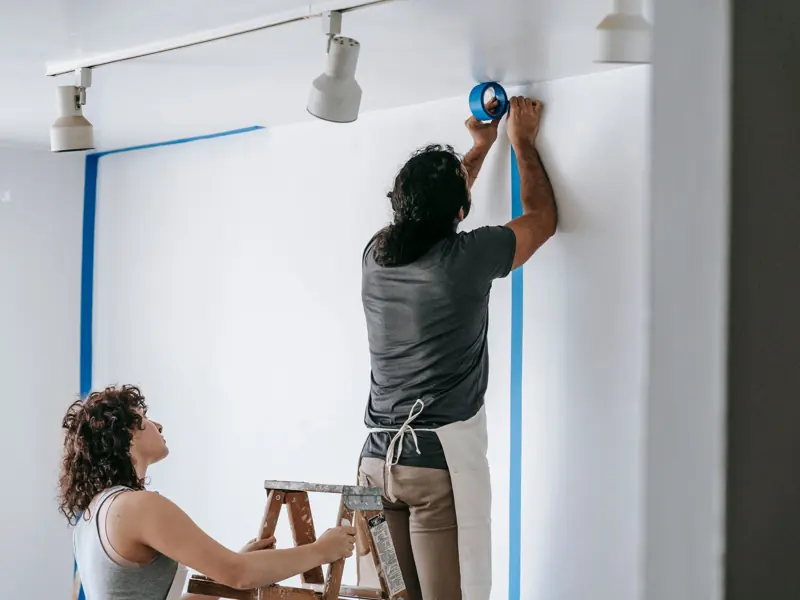 A man and woman working together on home renovation, applying painter's tape.