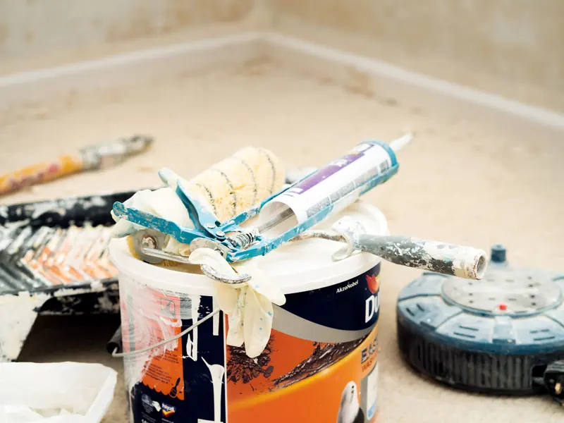 A collection of painting tools and materials for home renovation, featuring paint rollers and a bucket.