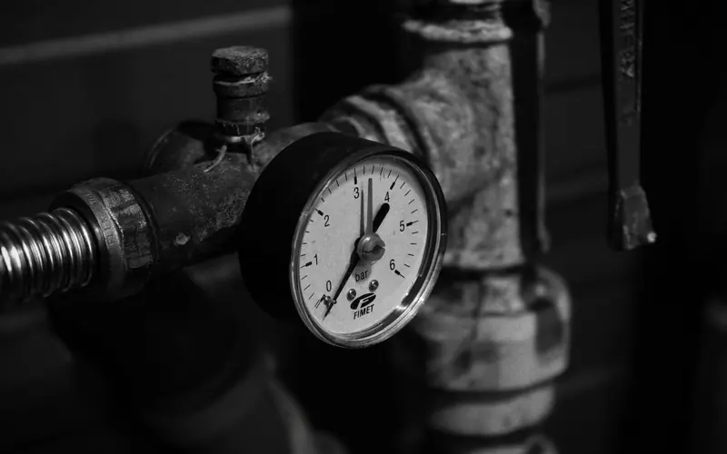 Close-up of a vintage pressure gauge on industrial pipes in monochrome.