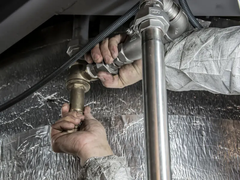 Close-up of a plumber's hands installing steel pipes indoors, showcasing skilled manual work.