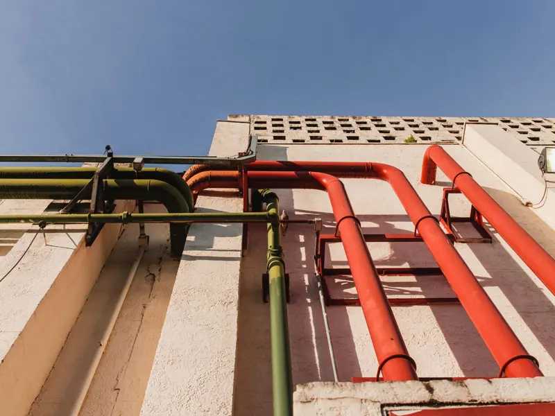 Close-up of vibrant red and green pipes on a sunlit urban building wall.
