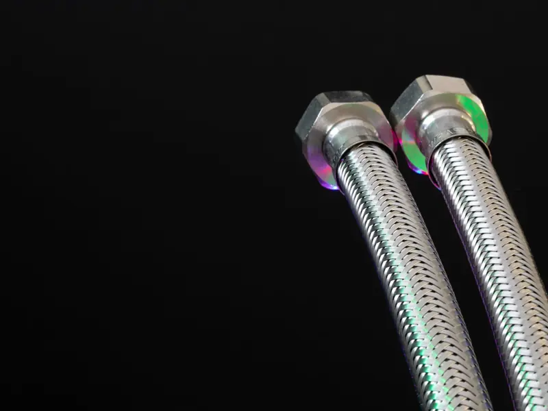 Close-up of metal flex pipes with hex nuts on a black background, showcasing industrial design.