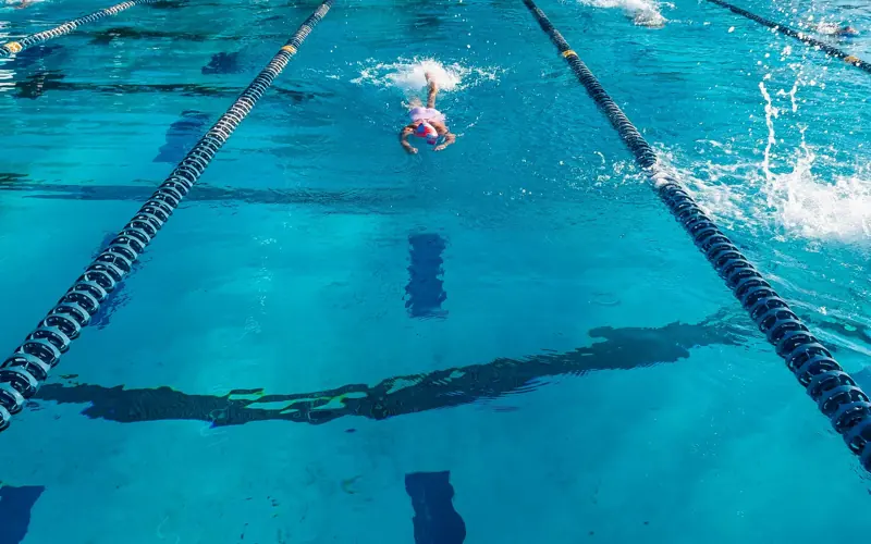 Young athlete swimming in a clear blue outdoor pool, focusing on competitive sport and fitness.
