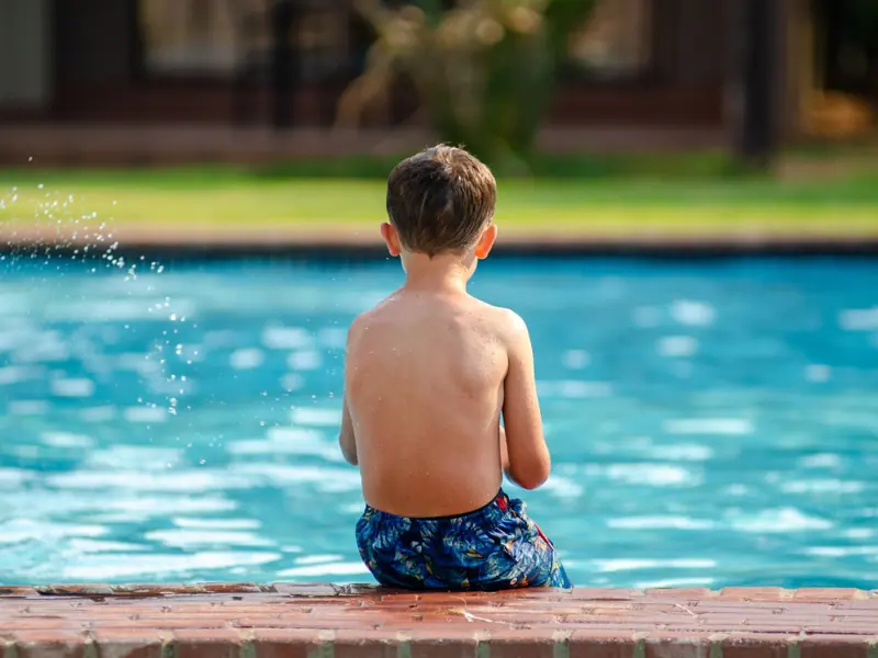 A child sits on the poolside, enjoying a sunny day outdoors.