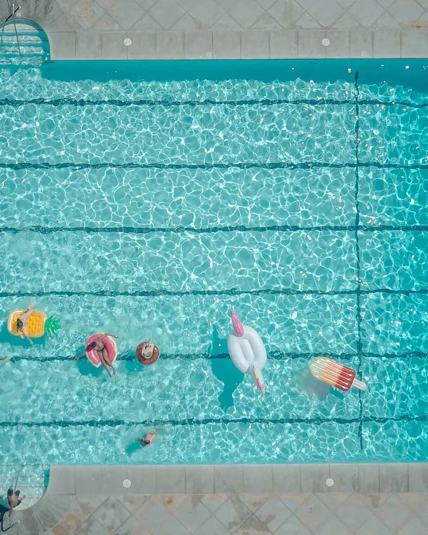Top-down view of a swimming pool with colorful floats and people enjoying a sunny pool party.