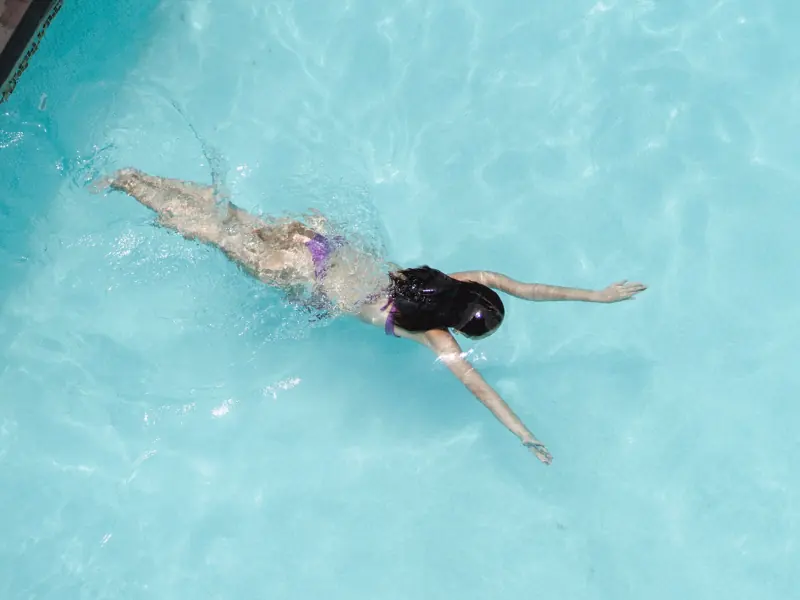 Top view of anonymous slim lady floating underwater in crystal clear blue water in swimming pool on resort