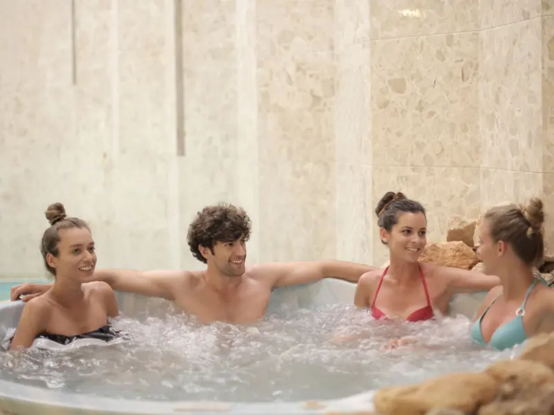 Four friends relaxing together in an indoor jacuzzi enjoying leisure time.