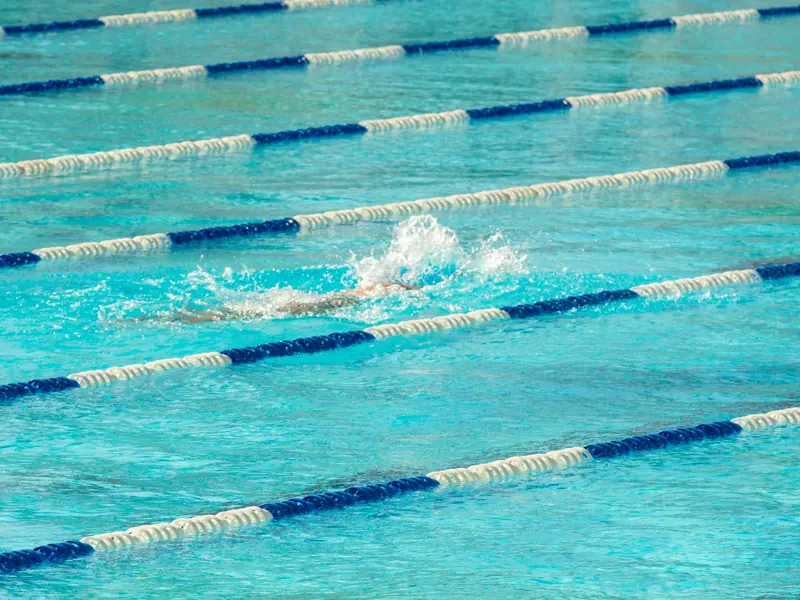 Swimmer in action making a splash in clear blue swimming pool lanes.