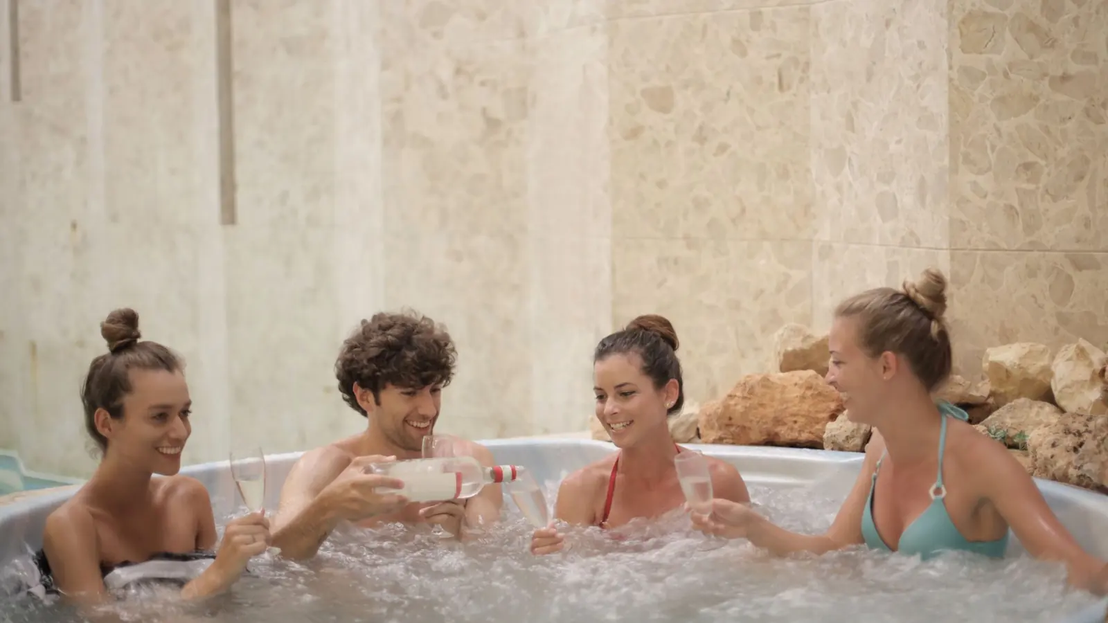 Friends having fun and relaxing together in a jacuzzi with drinks indoors.
