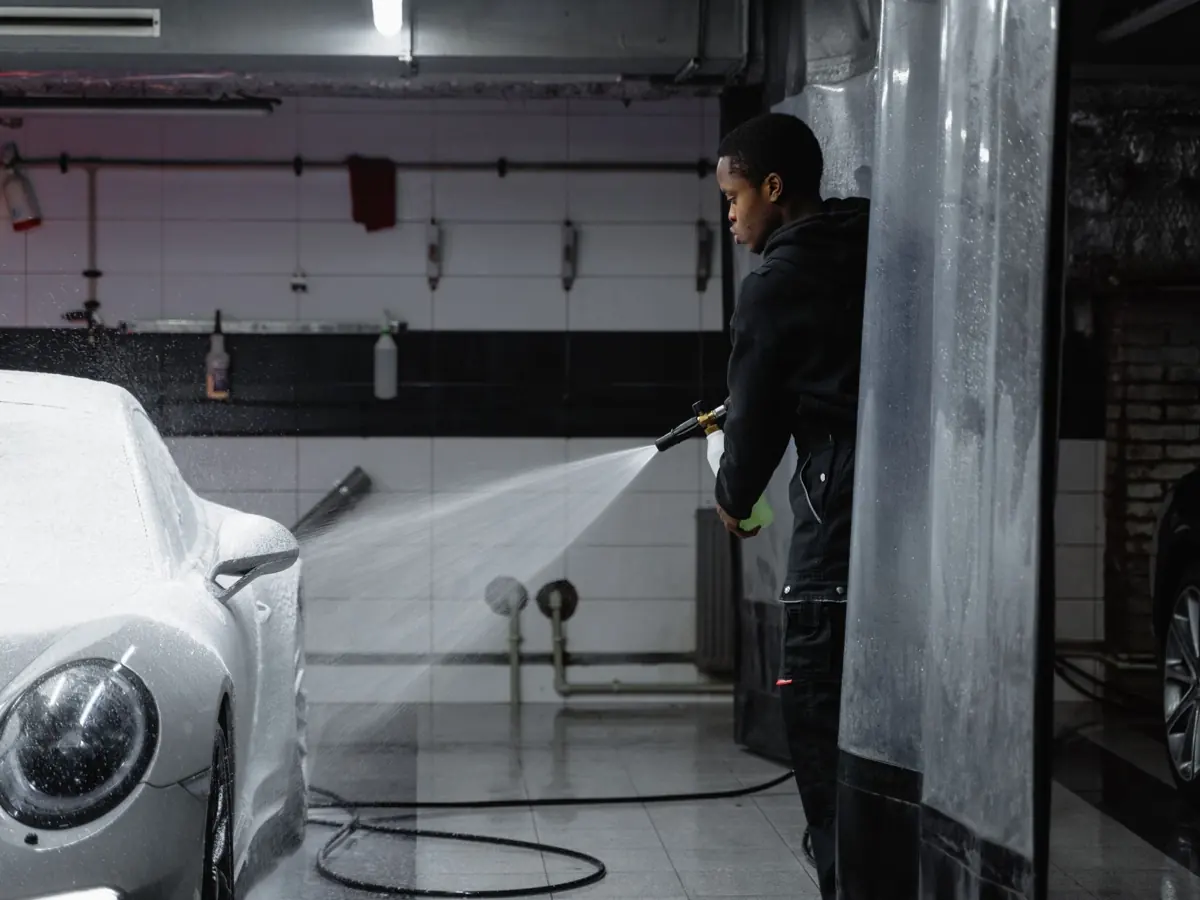 A person using a pressure washer to clean a car in an indoor garage setting.