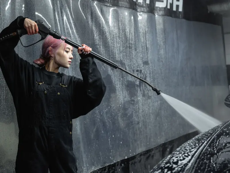 A woman using a pressure hose for car cleaning in an indoor garage.