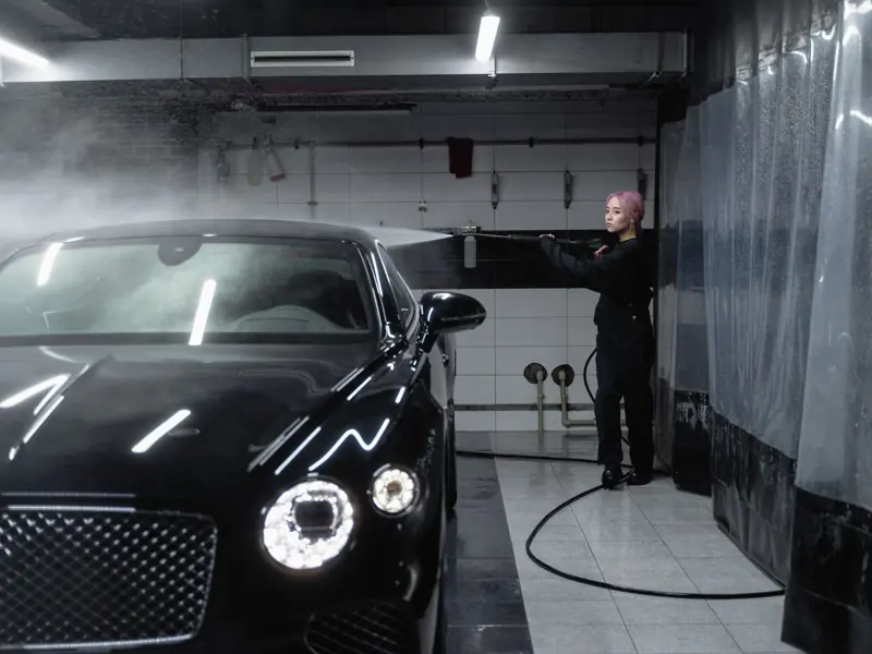 A woman using a power spray to wash a luxury car inside a garage, emphasizing precision and care.