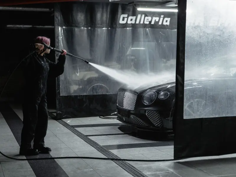 A woman power washing a luxury car in an indoor garage setting, showcasing car wash service.
