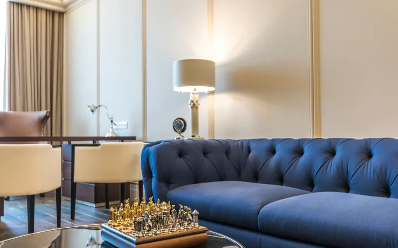 Stylish living room featuring a blue couch, chess set, lamps, and modern decor.