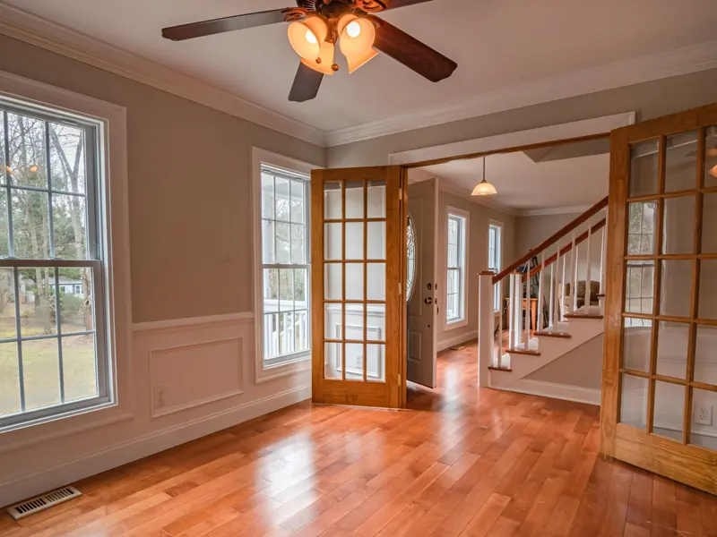 Spacious living room with wooden French doors and ceiling fan, showcasing contemporary interior design.
