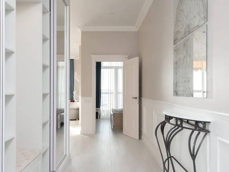 Hallway with empty opened wardrobe and mirror against wall with decorated white shelf in contemporary spacious light flat with rooms