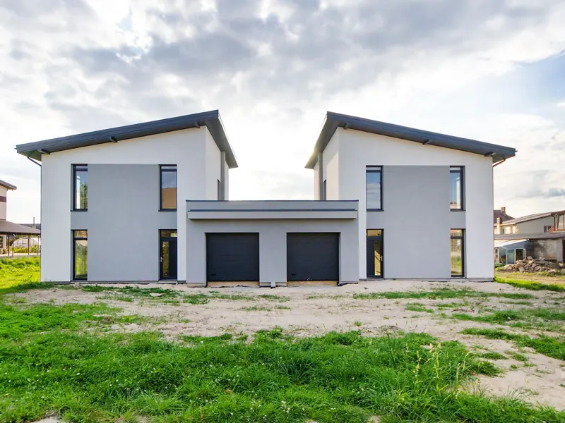 Front view of twin modern houses with a symmetrical architectural design under a cloudy sky.