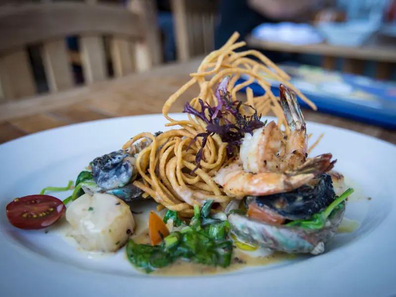 A gourmet seafood dish featuring grilled shrimp, creamy sauce, and fried noodles served on a white plate.