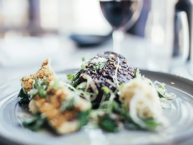 Tasty stuffed celery and grilled steak decorated with fresh green herbs served on plate on table in restaurant with wineglass on blurred background