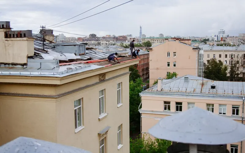 Construction workers repairing a rooftop in a vibrant cityscape.
