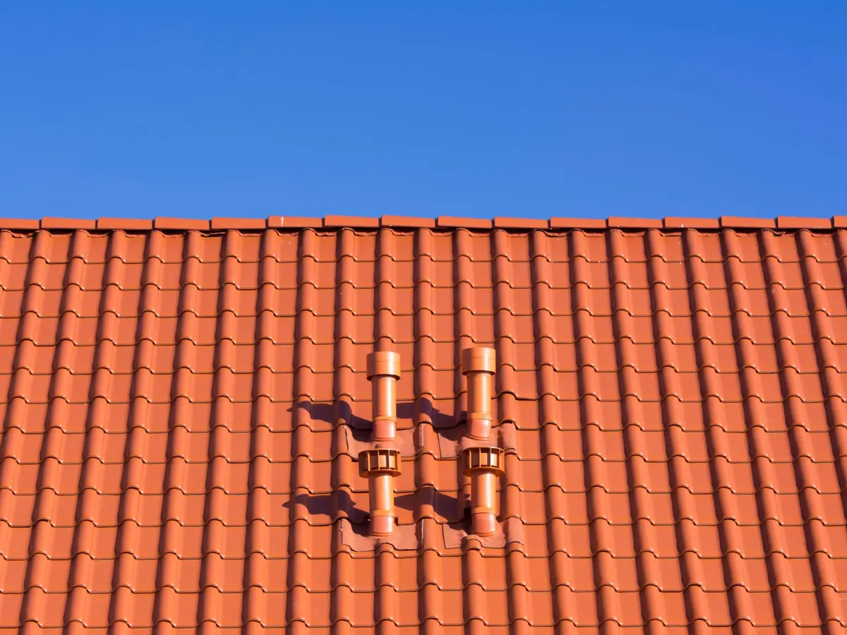 Vivid red clay rooftop with patterns and vents beneath a clear blue sky, ideal for architecture themes.