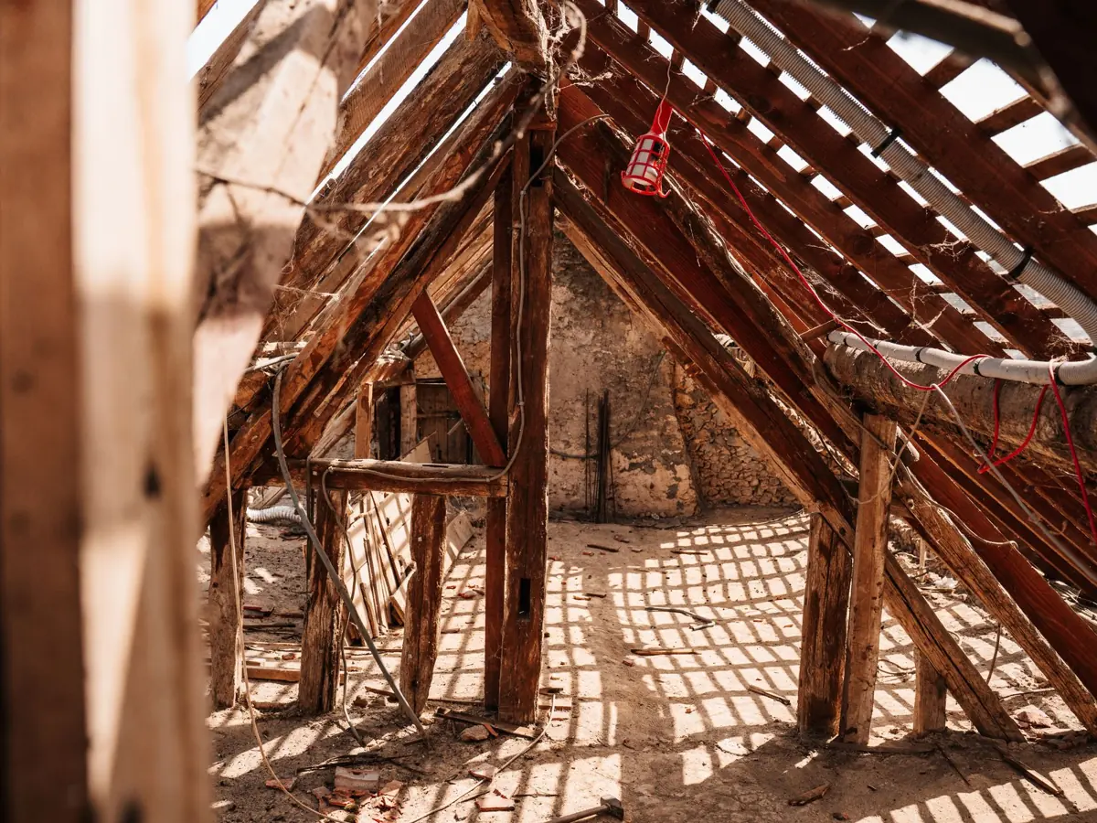 Interior view of wooden framing and rafters in a partially constructed attic space, highlighting a rustic and textured structure.