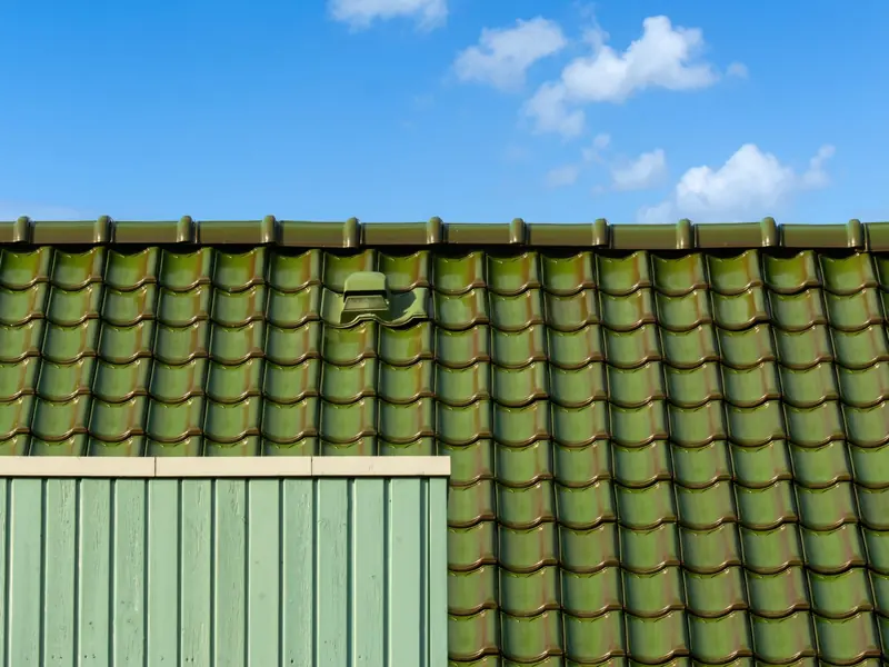 Closeup of a green tiled roof under a bright blue sky, capturing architectural detail and color contrast.