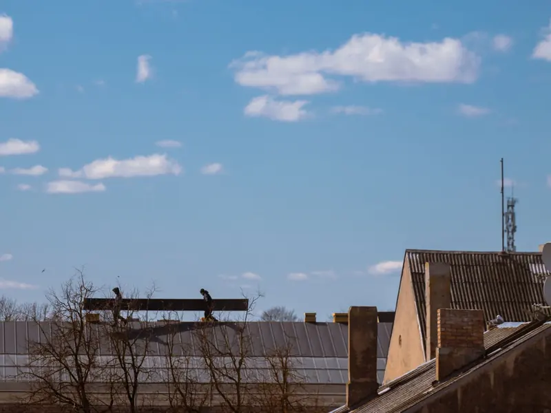 Silhouetted workers on a roof with clear blue sky and clouds in the background.