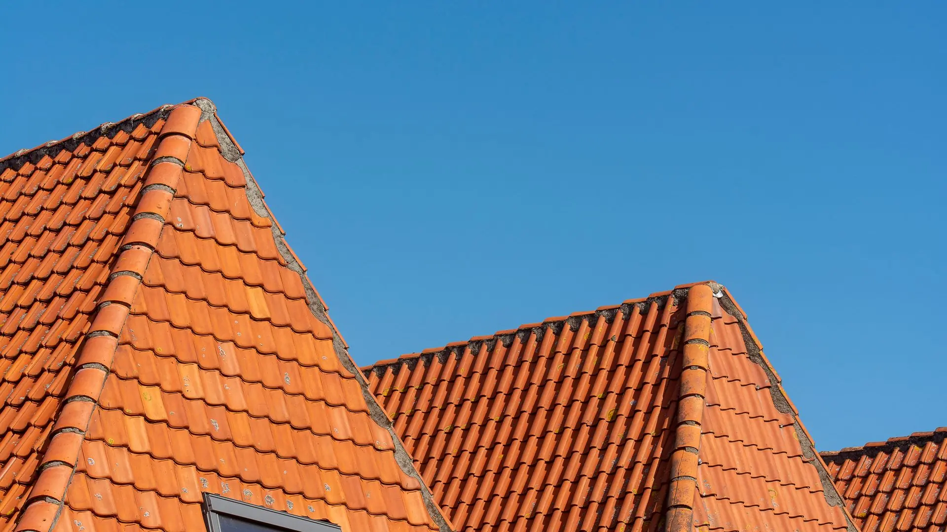Close-up of red tiled roofs under a clear blue sky, showcasing architectural design.