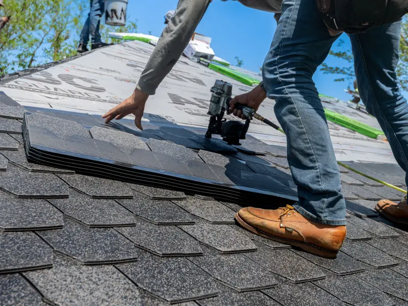 Roofer using nail gun for shingle installation on residential roof.