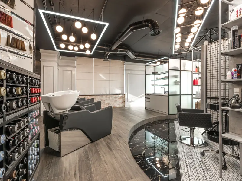 Black backwash chair with white sink placed in modern stylish beauty salon with various cosmetology products and bright glowing lamps