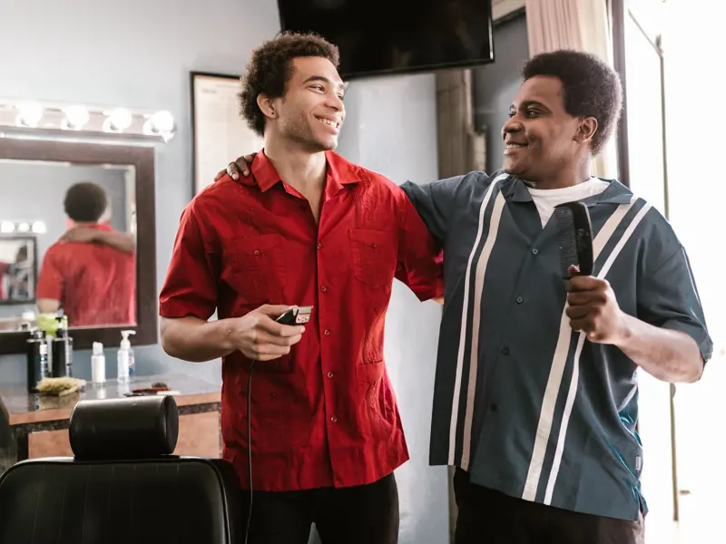 Two smiling barbers sharing a moment of camaraderie inside a barber shop.
