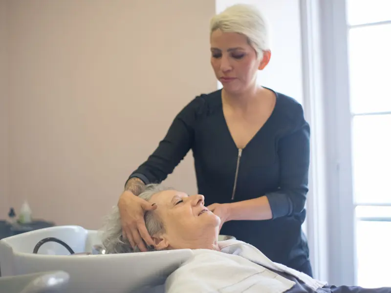 A hairdresser provides a relaxing washing service to an elderly woman in a salon.