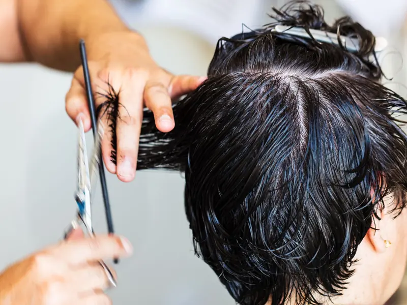 Close-up of a stylist cutting dark, wet hair in a salon setting, showcasing the precision and technique of hairstyling.