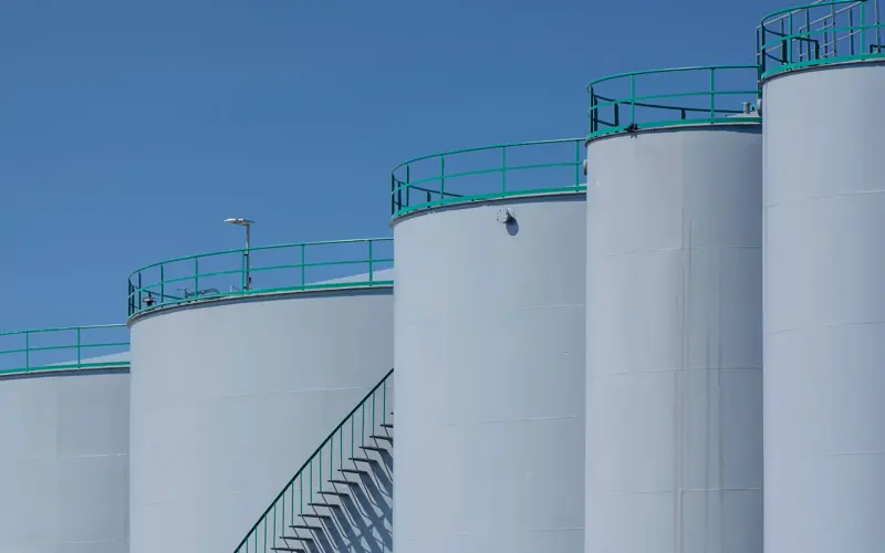 Large industrial storage tanks with green railings against a clear blue sky.