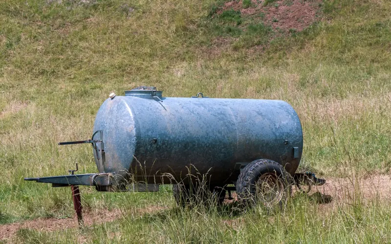 A rustic metal water tanker sits in a grassy field, ideal for agricultural themes.