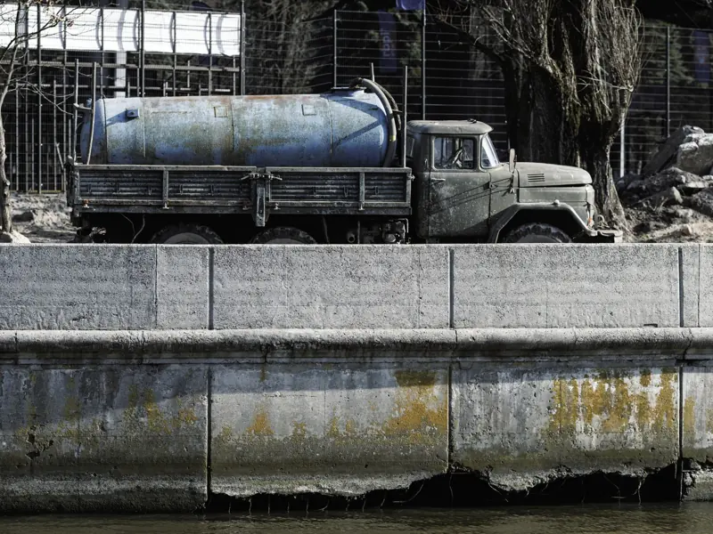 A vintage cement mixer truck parked by a canal with visible signs of wear and weathering.