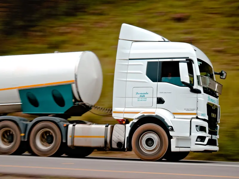 Close-up of a fast-moving white tanker truck on a highway, capturing motion and speed.