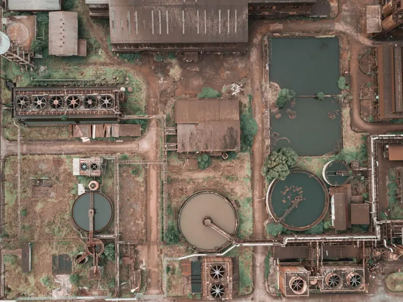Drone view of abandoned chemical plant with rusty and unused production buildings and round tanks with dirty water