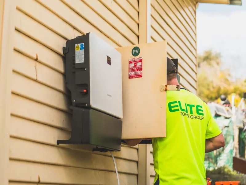 Electrician from Elite Power Group installing a solar inverter outside.
